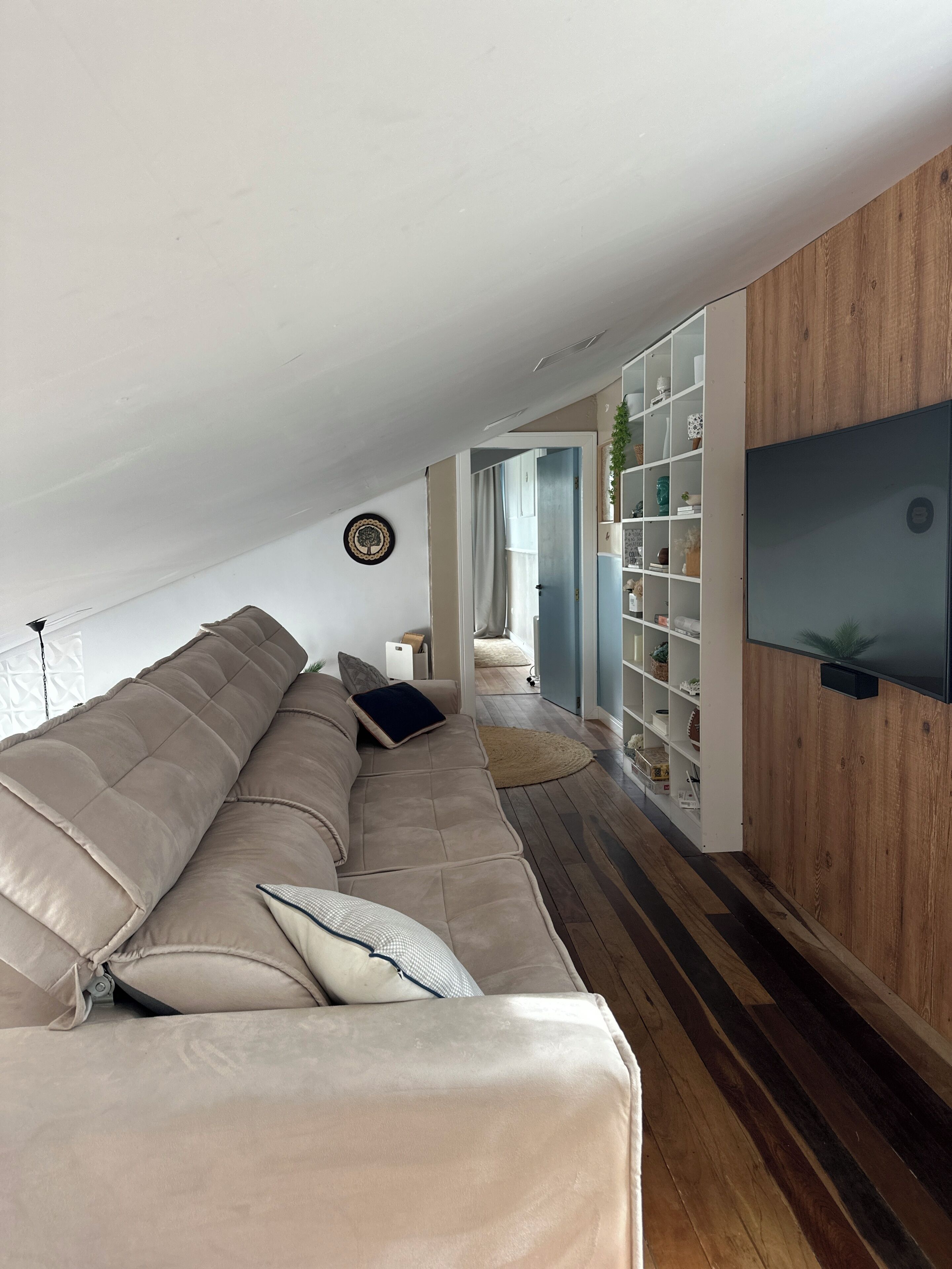 Ein modernes Wohnzimmer mit einem großen beigen Sofa, einem flachbildfernseher, der an einer Holzwand montiert ist, und Holzdielen.