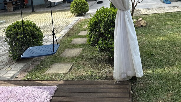 A covered outdoor area with a hammock, a swing, a pool, and a patio with a view of a building.