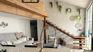 A modern kitchen with a central island, a wooden staircase, and a living area with a sofa and decorative wall art.