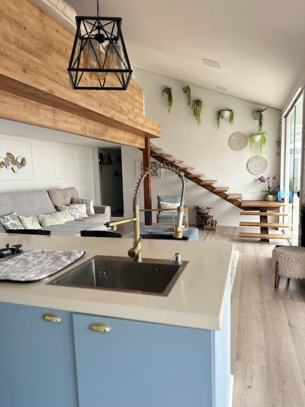 Une cuisine moderne dotée d’un îlot central, d’un escalier en bois et d’un espace de vie comprenant un canapé et des œuvres d’art décoratives murales.