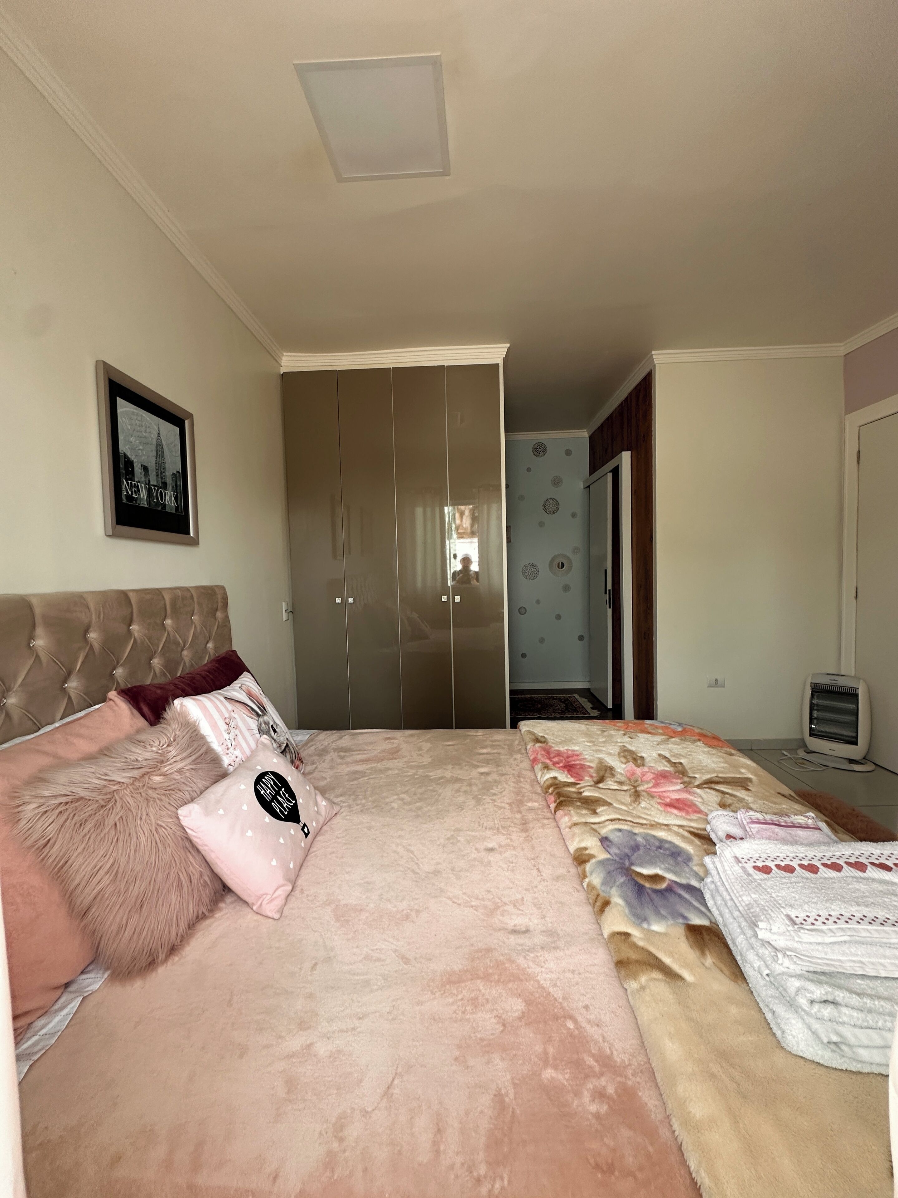 A bedroom with a bed, a wardrobe, a heater, and a framed picture on the wall.