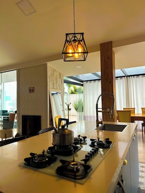 Une cuisine moderne dotée d’un îlot central, d’une cuisinière à gaz et d’un luminaire suspendu.