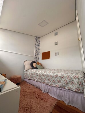 A bedroom with a bed, a fluffy rug, a desk, and a wall-mounted bulletin board.