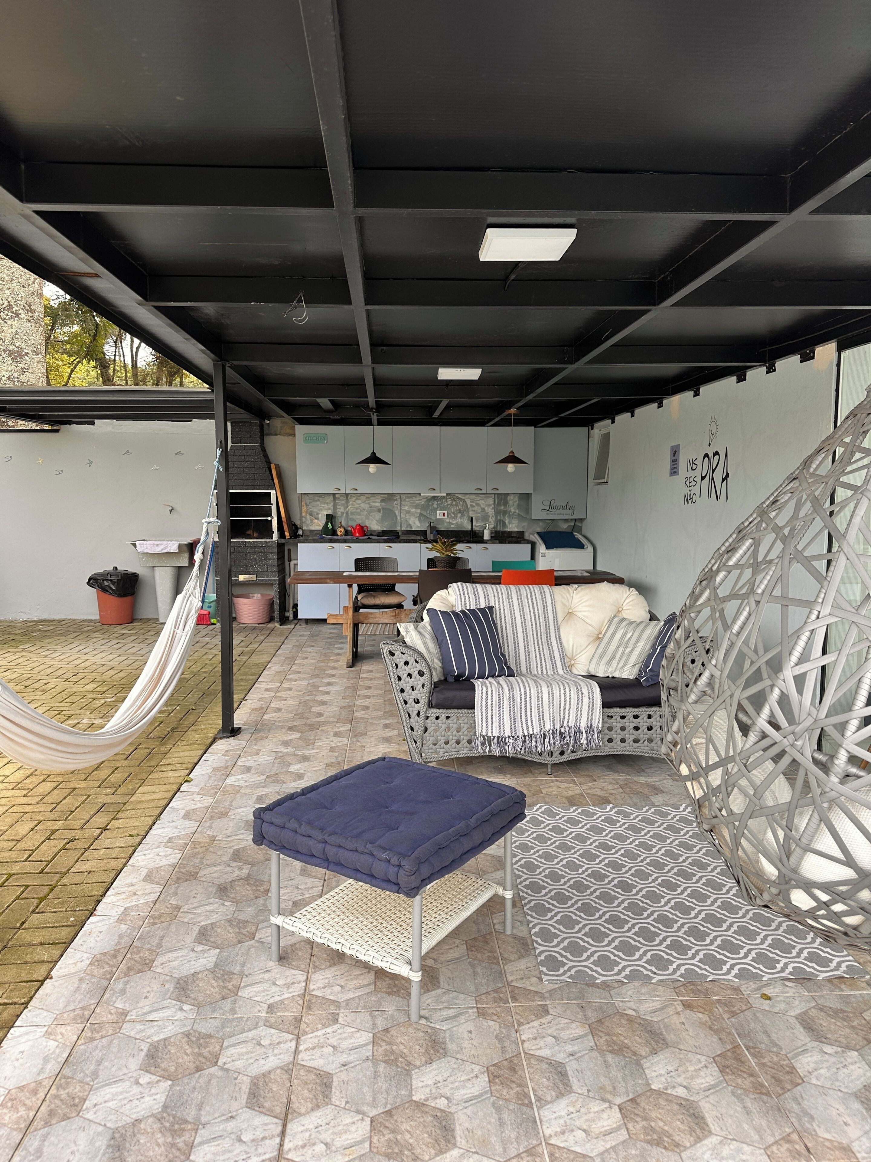 A covered outdoor living area with a kitchen, seating, and a hammock.