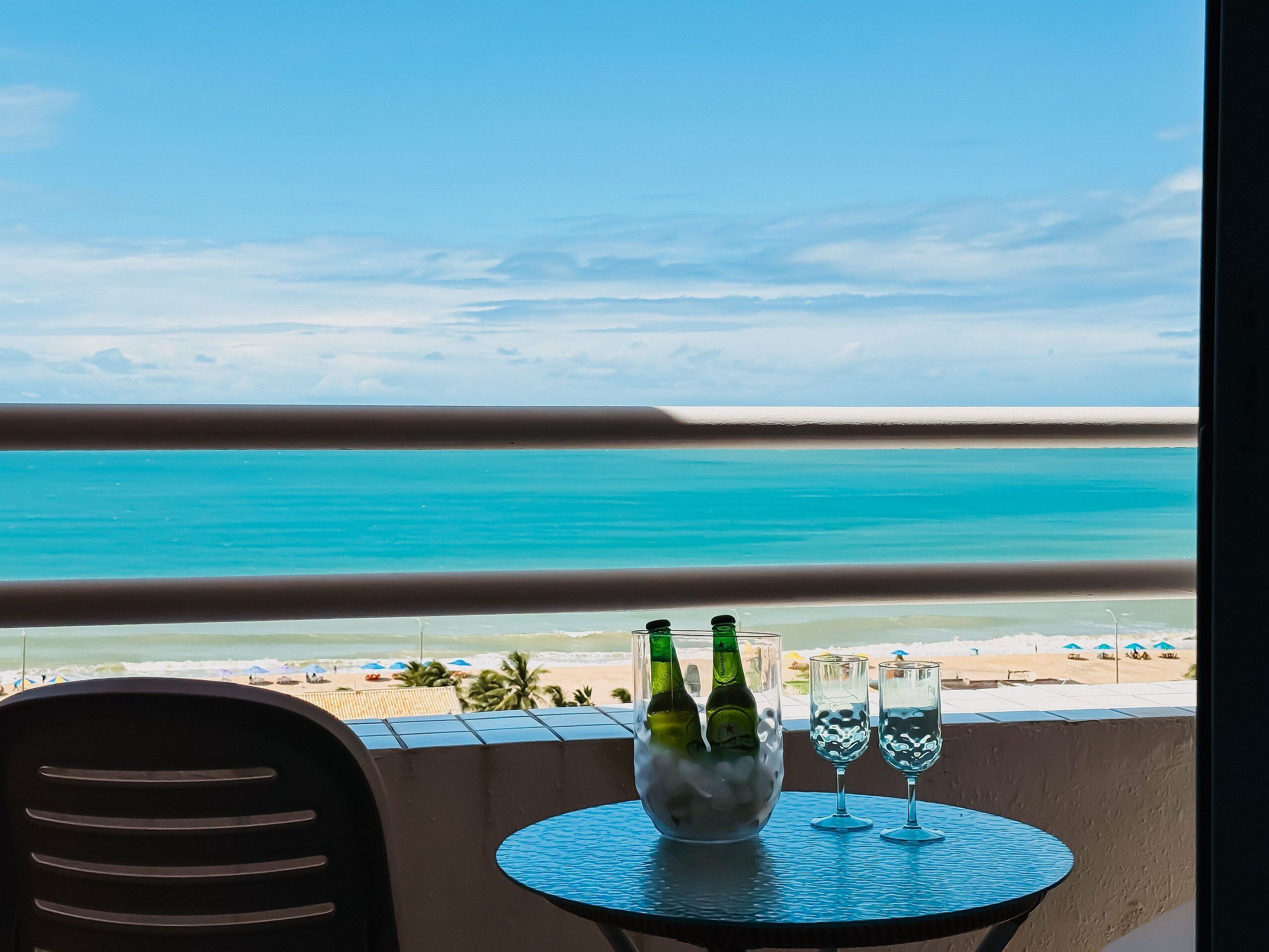 Ein Balkon mit Blick auf den Strand, ein Tisch mit zwei Flaschen und zwei Gläsern.