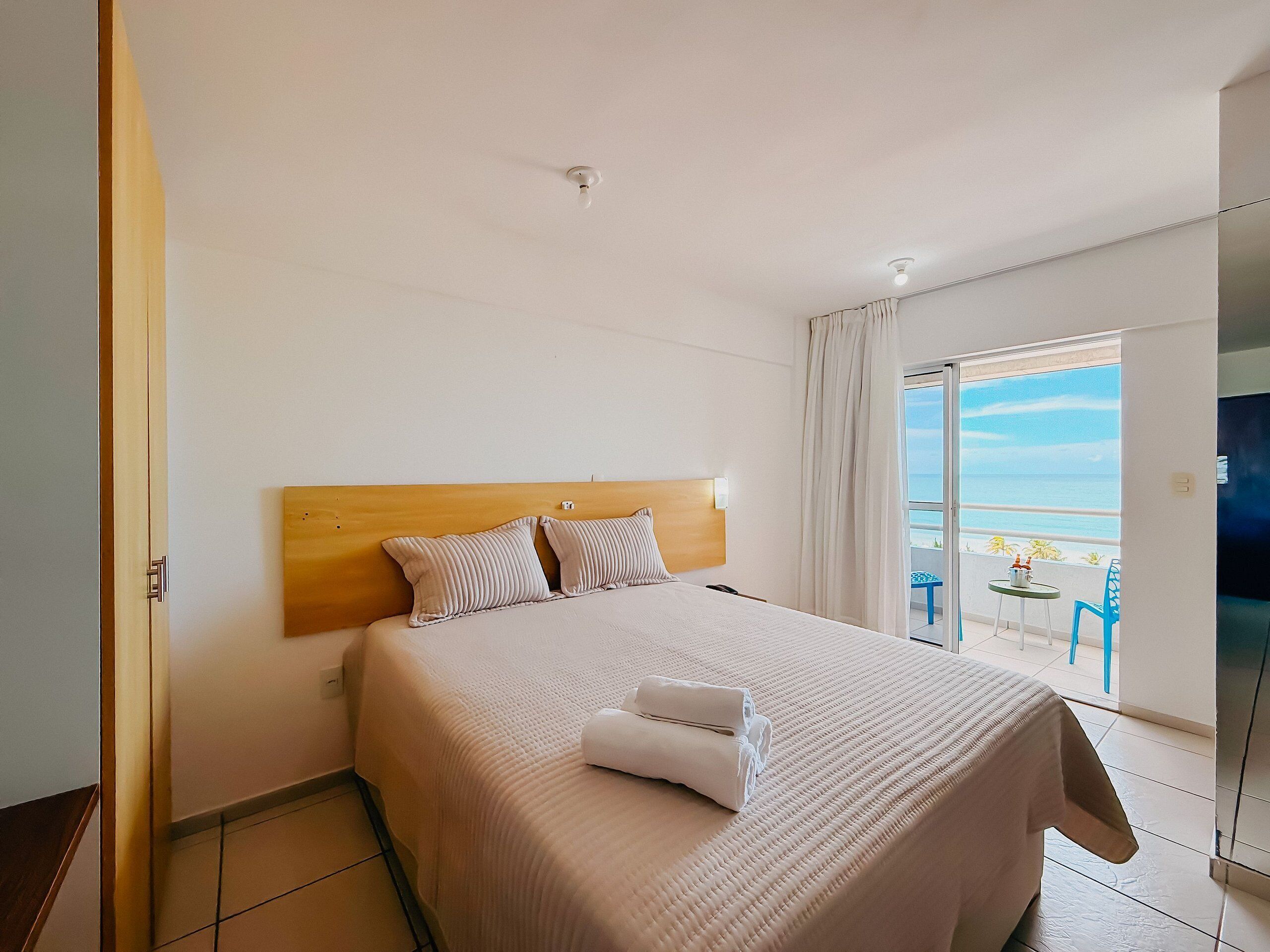 Une chambre d’hôtel avec un lit, un balcon donnant sur la mer et une porte située sur le côté gauche.