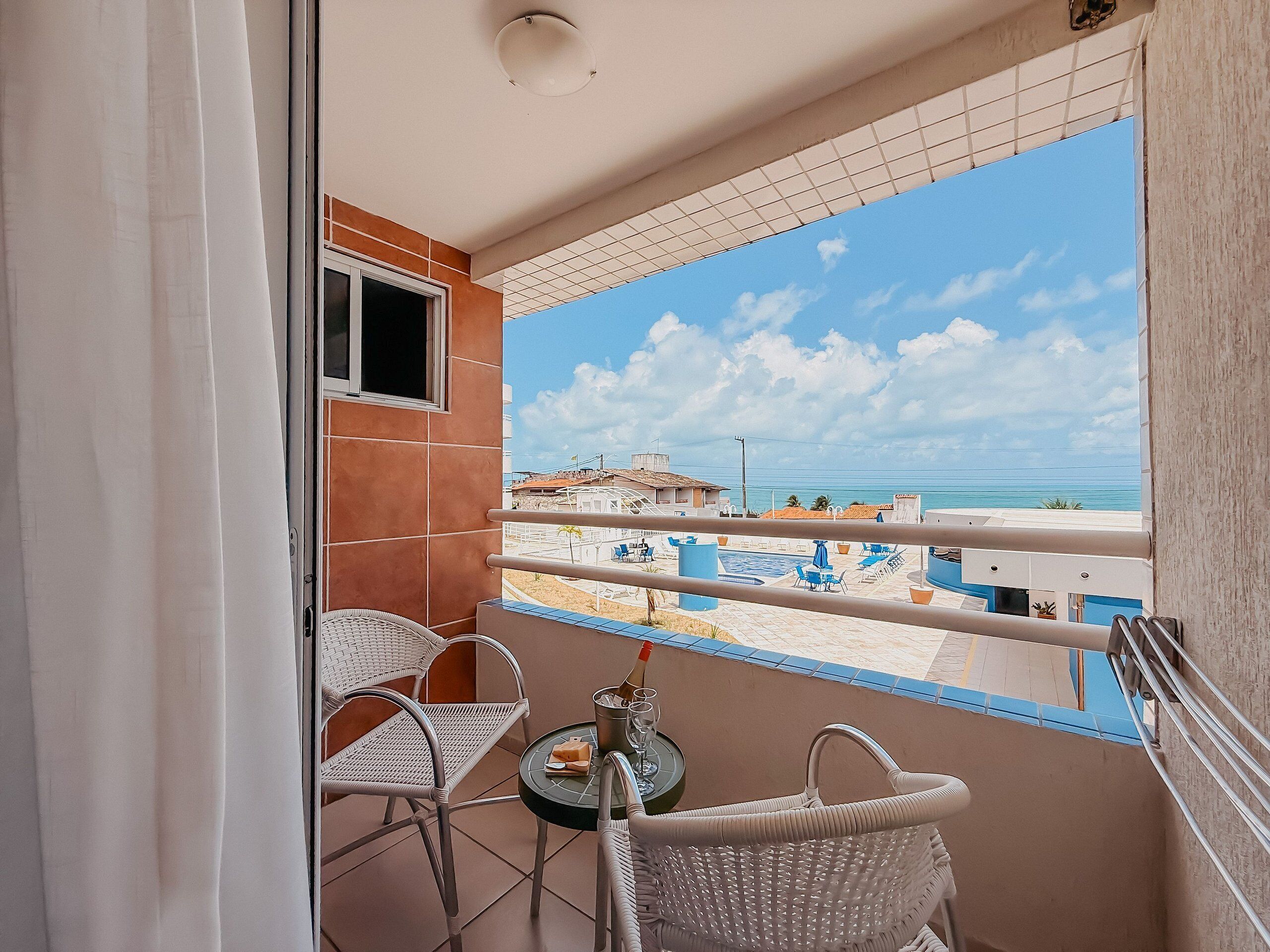 A balcony with a view of a swimming pool and buildings, a small table with a chair, and a window.