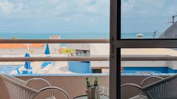 Un balcone con sedie in vimini, un tavolino con bottiglie e bicchieri, e vista su piscina e spiaggia.