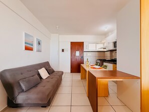 A compact living space with a sofa, a dining table, and a kitchenette. - Terrazo Ponta Negra by Almare (Natal)