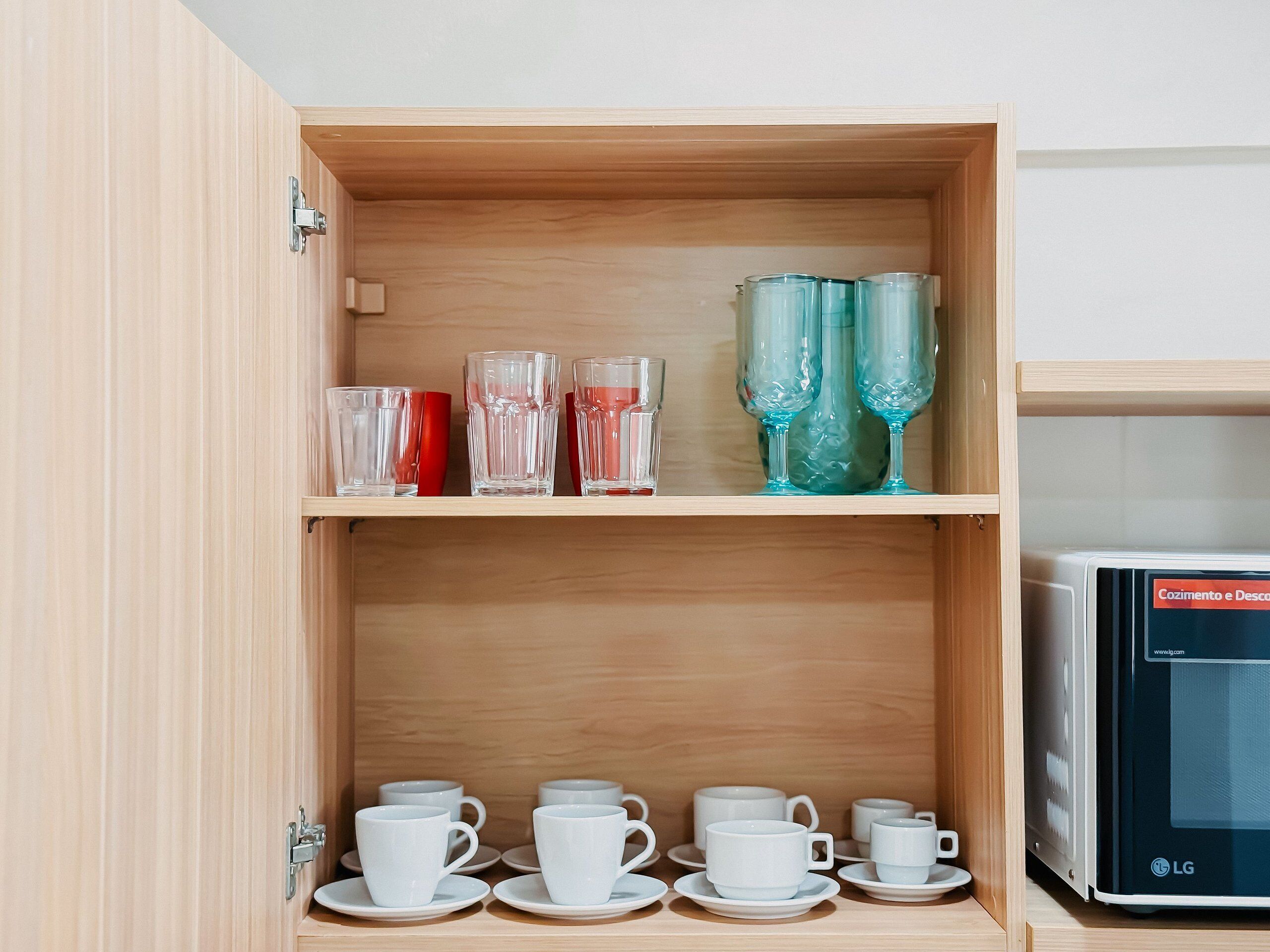 Een houten kast met planken, gevuld met divers glaswerk en witte bekers.