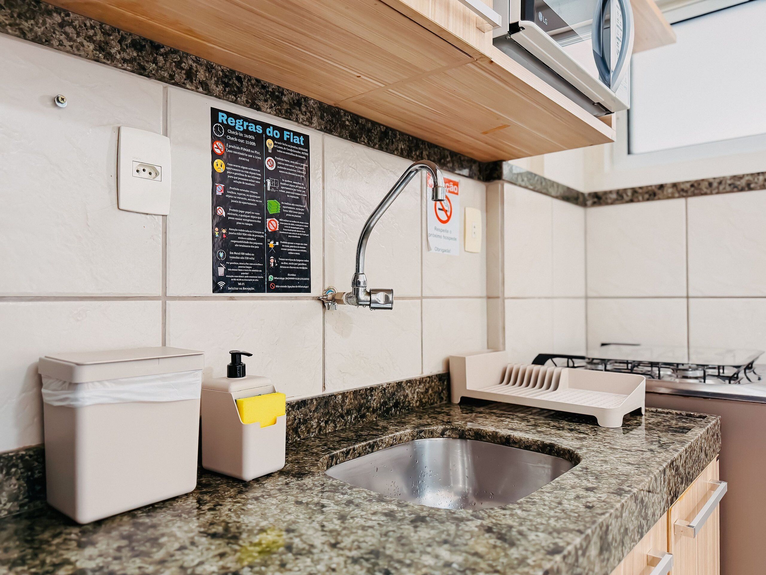 A modern kitchen with a granite countertop, stainless steel sink, and a blackboard with rules.