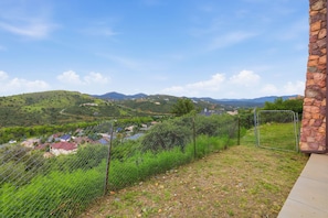 A fenced outdoor area with a stone wall, a clear view of a hilly landscape, and a distant village. - Cozy 1BR casita with stunning panoramic views (Prescott)