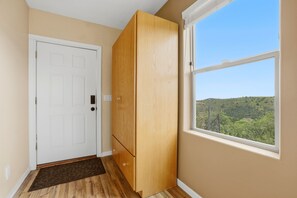 A room with a white door, a wooden wardrobe, a window with a view of a green landscape, and a brown doormat. - Cozy 1BR casita with stunning panoramic views (Prescott)