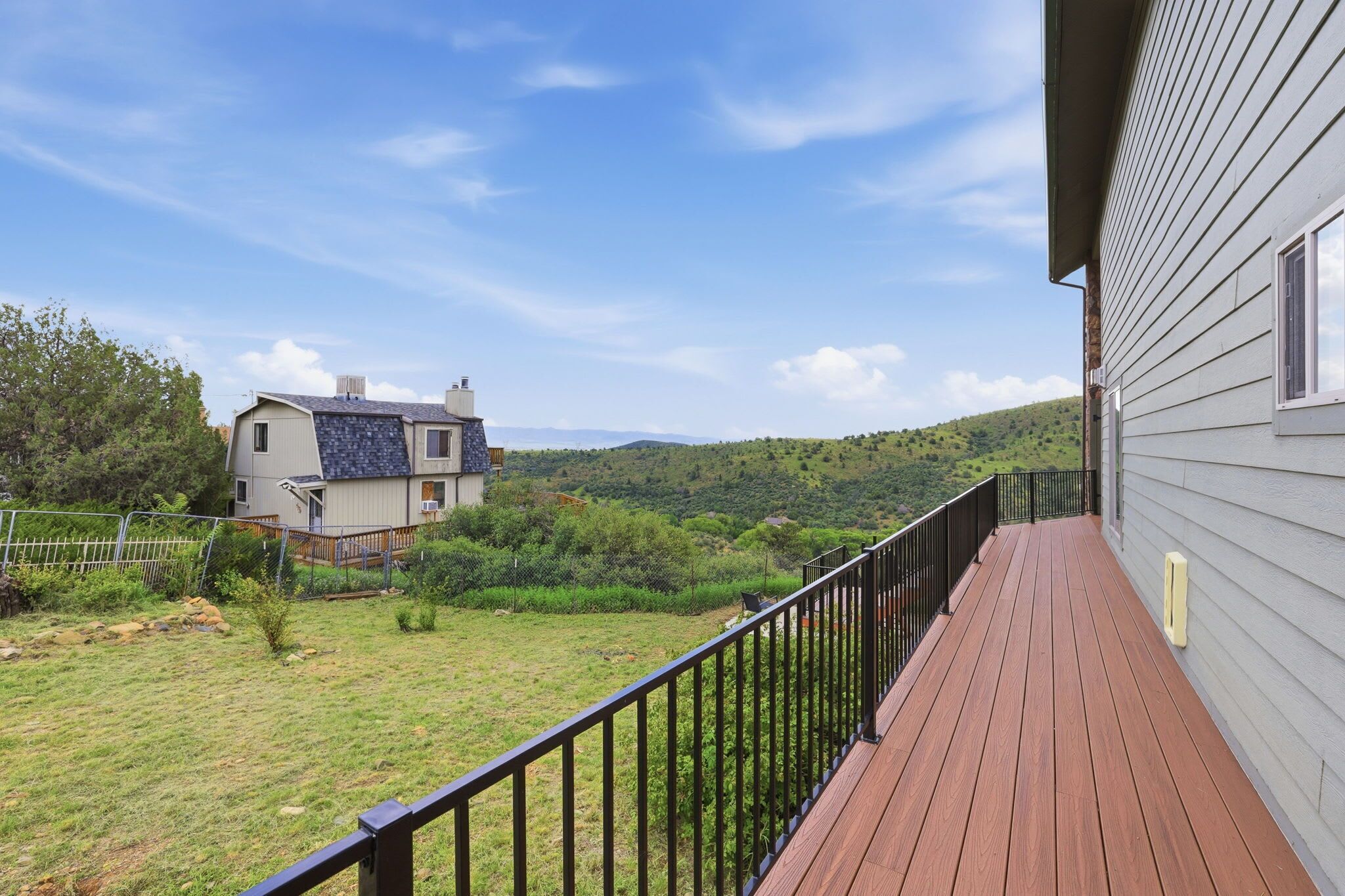 A wooden deck with a metal railing overlooking a grassy yard and a house with a sloped roof.