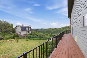 Une terrasse en bois avec une rambarde en métal, donnant sur une pelouse et une maison dont le toit est en pente.