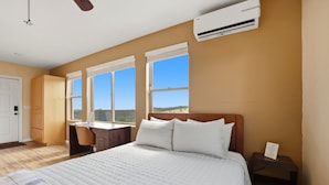 Ein Schlafzimmer mit einem Bett, einem Schreibtisch und einem Stuhl. An der Wand ist eine Klimaanlage angebracht.