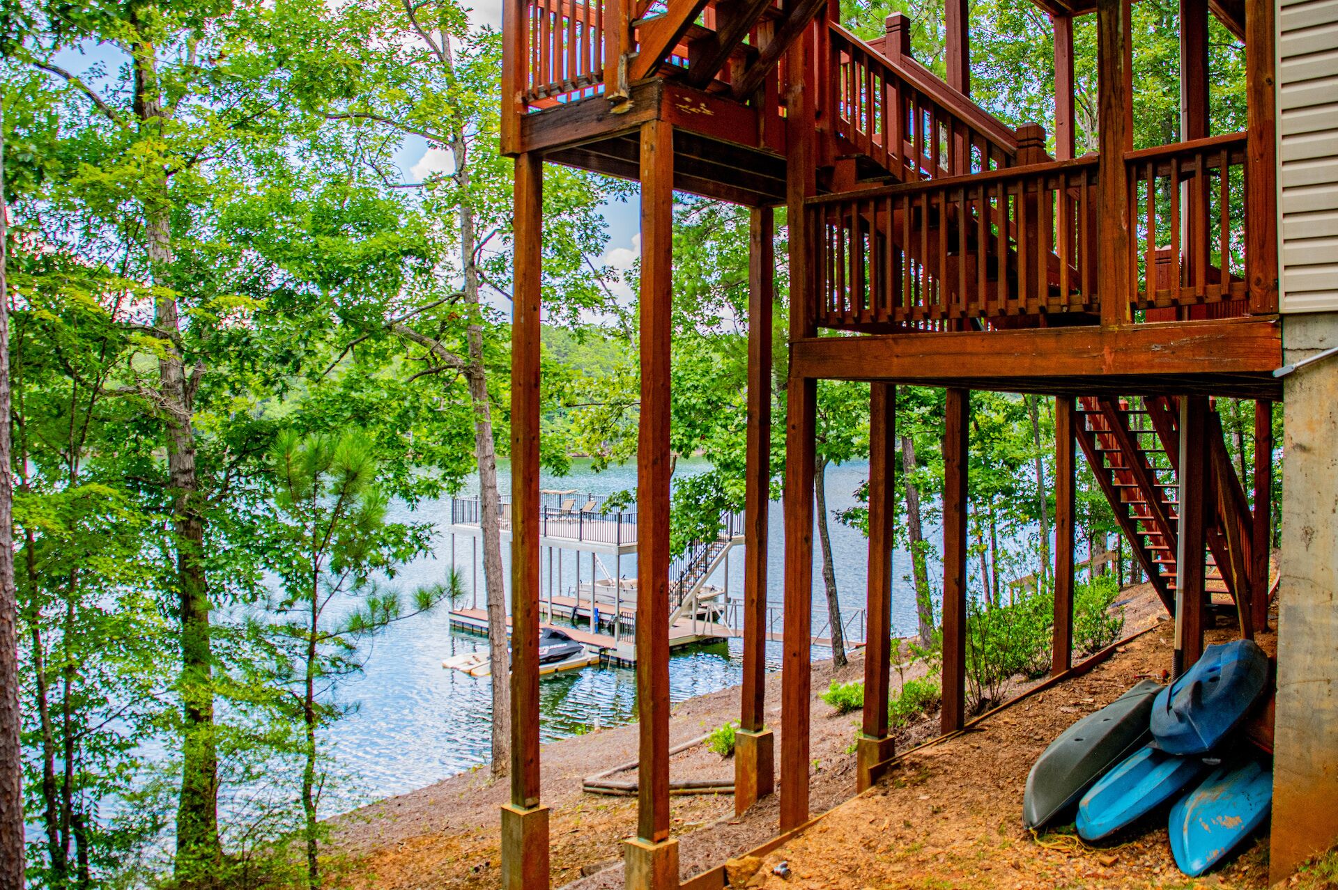 A wooden deck with a staircase leading to a dock over water, surrounded by trees.