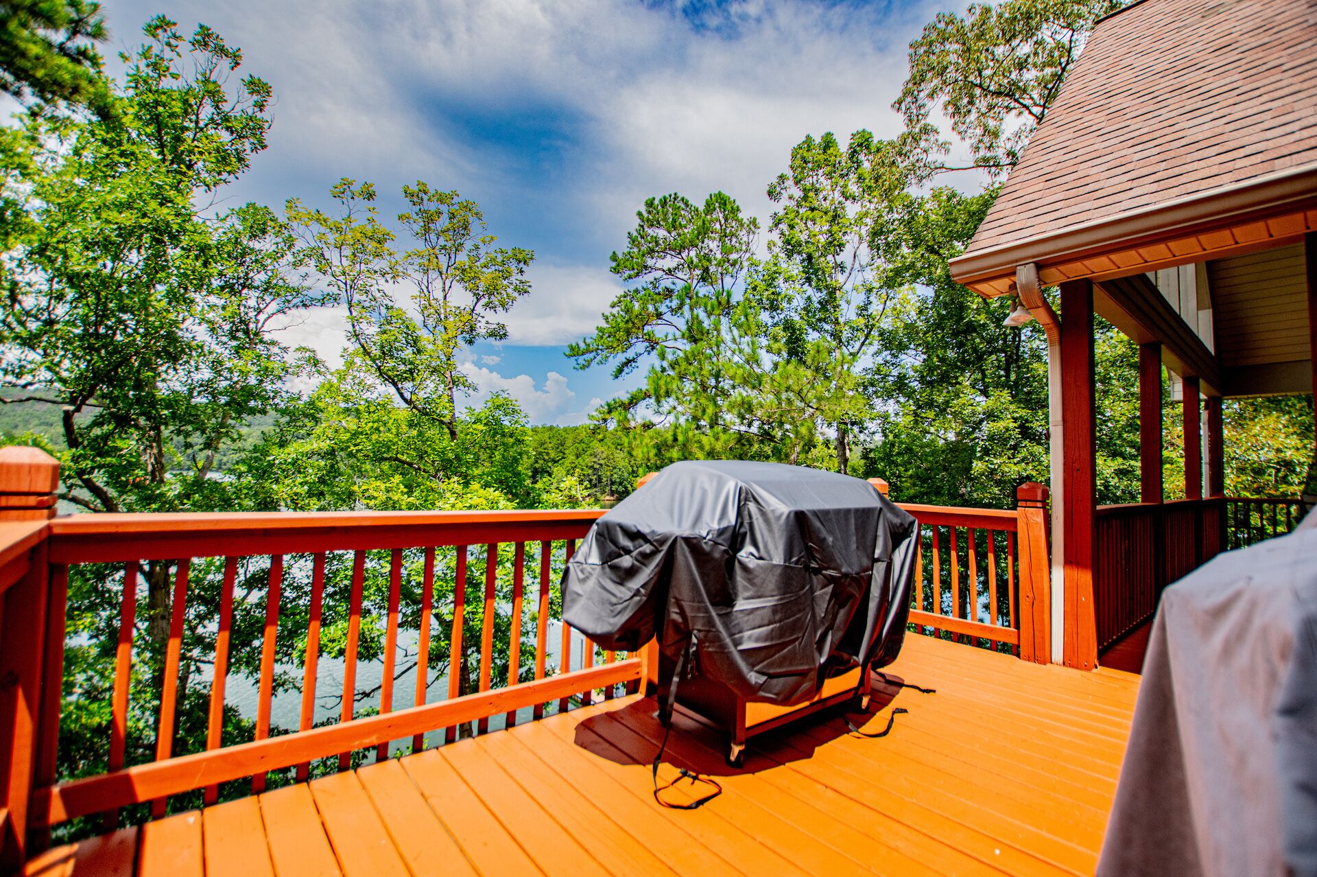 A covered grill on a wooden deck with a railing, overlooking a forested area.