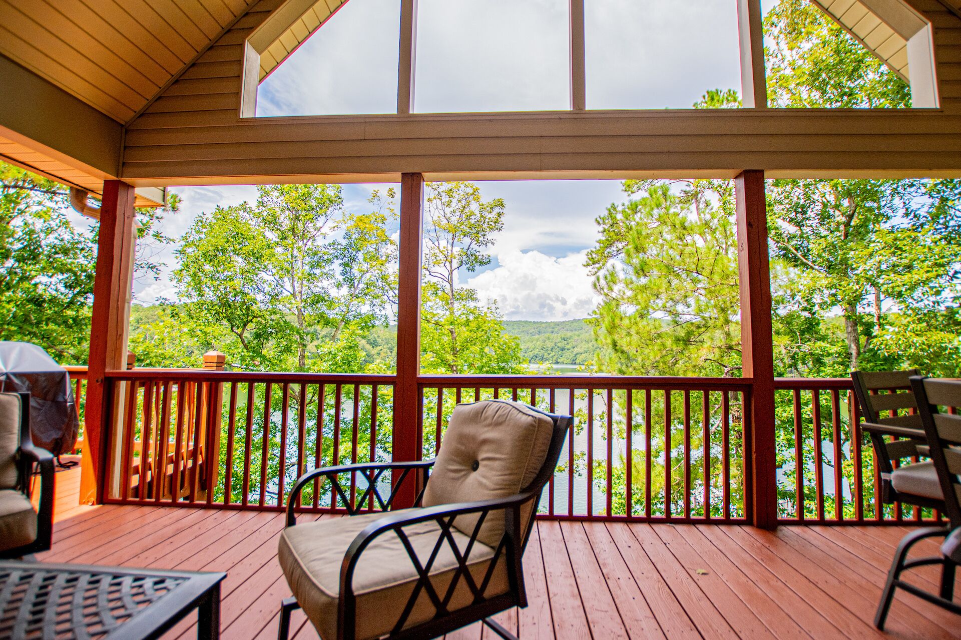 A covered outdoor deck with a view of a lake and trees.