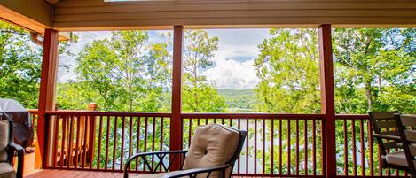 A covered outdoor deck with a view of a lake and trees.