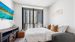 A modern bedroom with a bed, a TV, a window with a city view, and a decorative wall piece. - Bright & Modern Downtown Miami – 1BR 501 First #1406 (Miami)