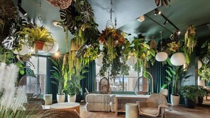 A room with a high ceiling, hanging plants, wicker furniture, and a view of the city. - Bright & Modern Downtown Miami – 1BR 501 First #1406 (Miami)