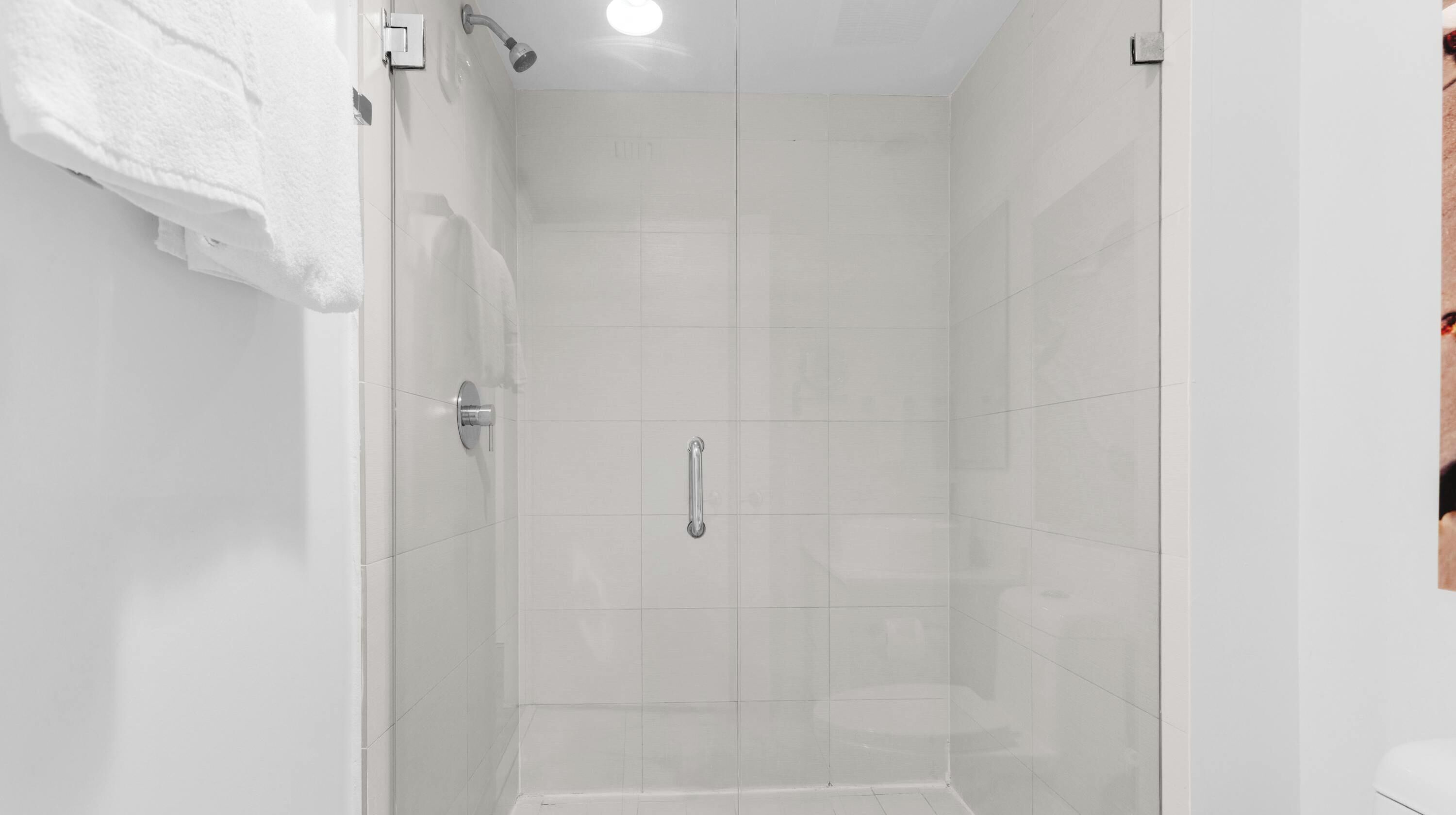 Un baño moderno con cabina de ducha de vidrio, una toalla blanca en la pared y un cabezal de ducha visible.