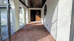 Un corridoio con pavimento in mattoni, pareti bianche e soffitto in legno.