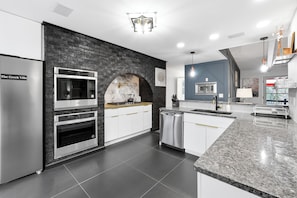 Eine moderne Küche mit Akzentwand aus Stein, integrierten Geräten und einer Arbeitsplatte aus Granit.