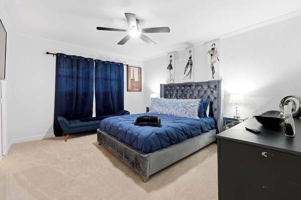 Ein Schlafzimmer mit einem Bett, einem blauen Sofa, einem Schreibtisch, einem Deckenventilator und Bildern an der Wand.