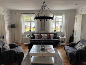 A living room with a dark sofa set, a glass coffee table, and a chandelier.