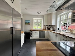 A modern kitchen with a stainless steel refrigerator, white cabinetry, a wooden countertop, and a window with a view of greenery.