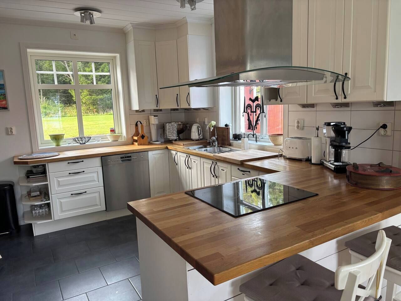 A modern kitchen with white cabinetry, a wooden countertop, and a large window.