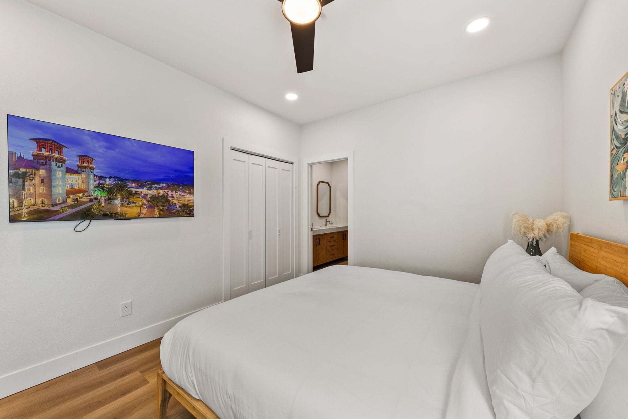A bedroom with a large bed, a nightstand, a mirror, and a painting of a cityscape.