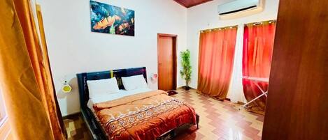 A room with a bed, a potted plant, an air conditioning unit, and a painting on the wall.