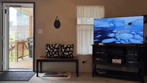 A living room with a television displaying a snowy landscape, a wooden bench, and a door leading to a balcony.