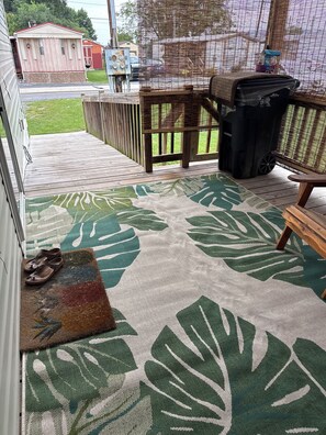 A covered outdoor area with a wooden deck, a bench, a trash bin, and a covered table. - Cozy 2-bedroom mobile home in Moorefield with AC/ WiFi (Moorefield)