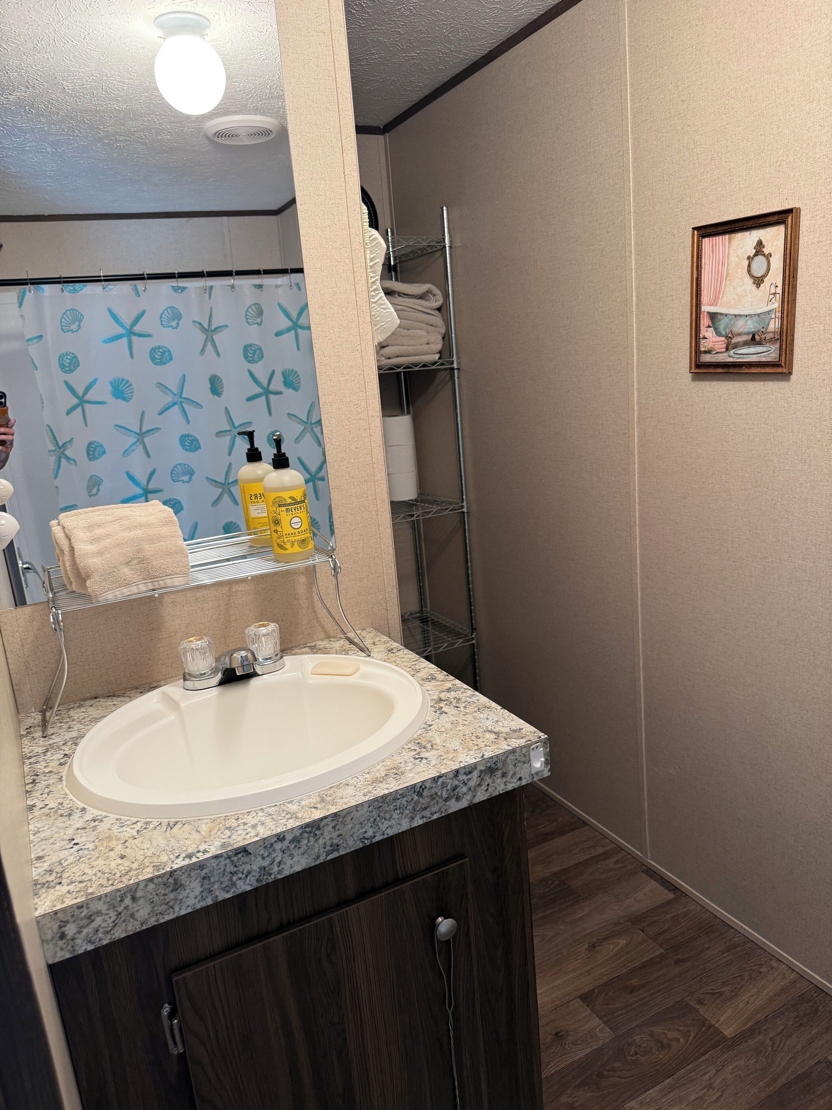 Une salle de bain avec un lavabo sur un plan de travail en granit, un porte-serviettes et un rideau de douche orné d’un motif d’étoile de mer.