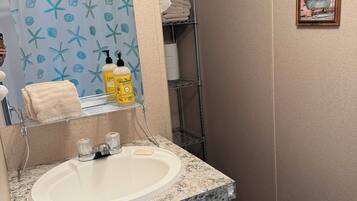 Une salle de bain avec un lavabo sur un plan de travail en granit, un porte-serviettes et un rideau de douche orné d’un motif d’étoile de mer.