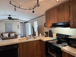 Cocina compacta con armarios de madera, estufa negra y encimera de granito.