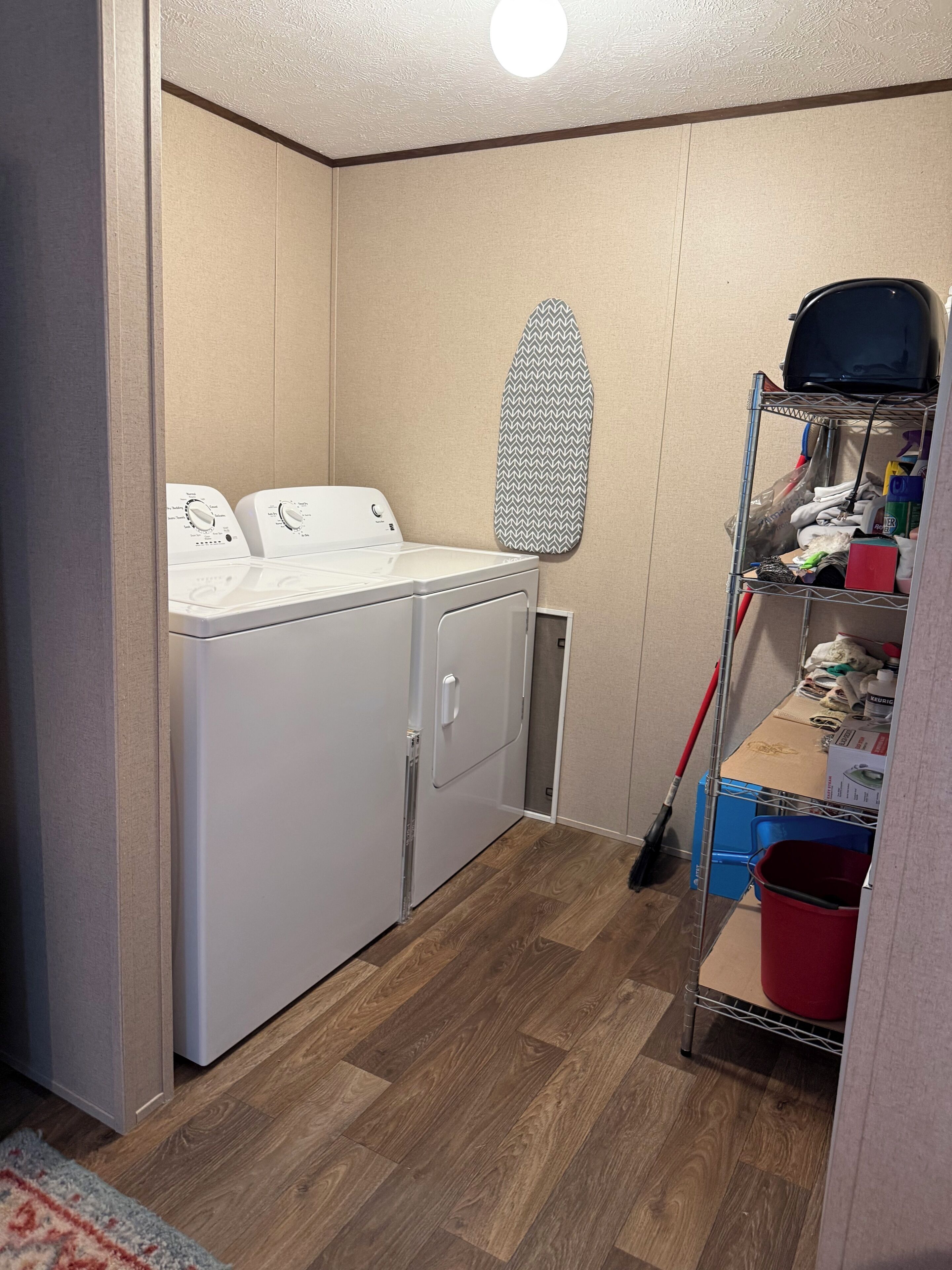 A laundry room with a washing machine, a drying rack, and a storage shelf with cleaning supplies.