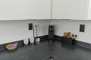 Eine moderne Küche mit weißen Schränken, einer Kaffeemaschine und einem Besteckhalter.