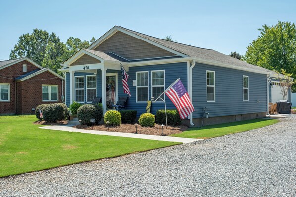 A residential house with a front porch, two flags, and a well-maintained lawn.