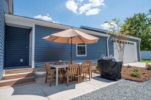 A patio with a table and chairs, a covered grill, and a blue house. - The Sweet Retreat is an amazing 3-bed/3 bath home in Concord, NC! (Concord)