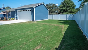 Quintal residencial com uma garagem azul, cerca branca e gramado bem cuidado.