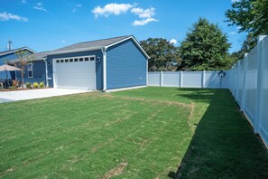 A residential backyard with a blue garage, a white fence, and a well-maintained lawn. - The Sweet Retreat is an amazing 3-bed/3 bath home in Concord, NC! (Concord)