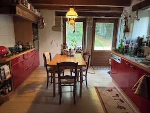 A kitchen with a wooden table and chairs, a hanging light fixture, and a view of greenery outside.