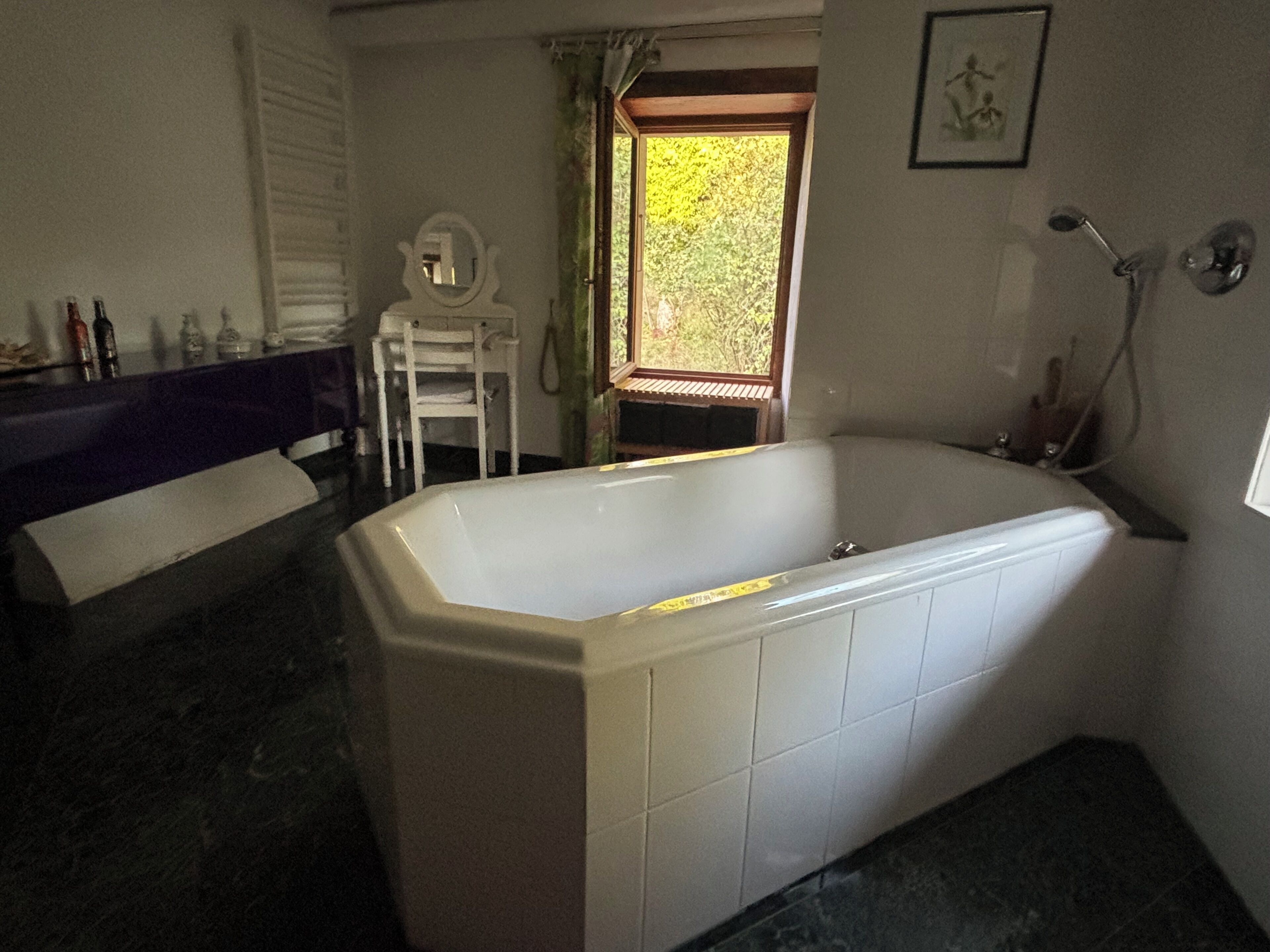 A bathroom with a large bathtub, a white sink, and a mirror. There is a window with a view of greenery outside.