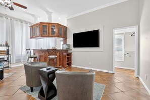 A modern living room with a wooden cabinet, a flat-screen TV mounted on the wall, and a dining area with a kitchen in the background. - Cozy Abilene Studio with Fireplace ~ Pet Friendly (Abilene)