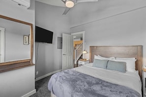 Ein Schlafzimmer mit einem Bett, einem an der Wand montierten Fernseher, einem Deckenventilator und einer Treppe, die zu einer oberen Ebene führt.